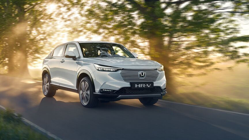 Trojštvrťový záber spredu na hybridný model HR-V pri jazde po vidieku