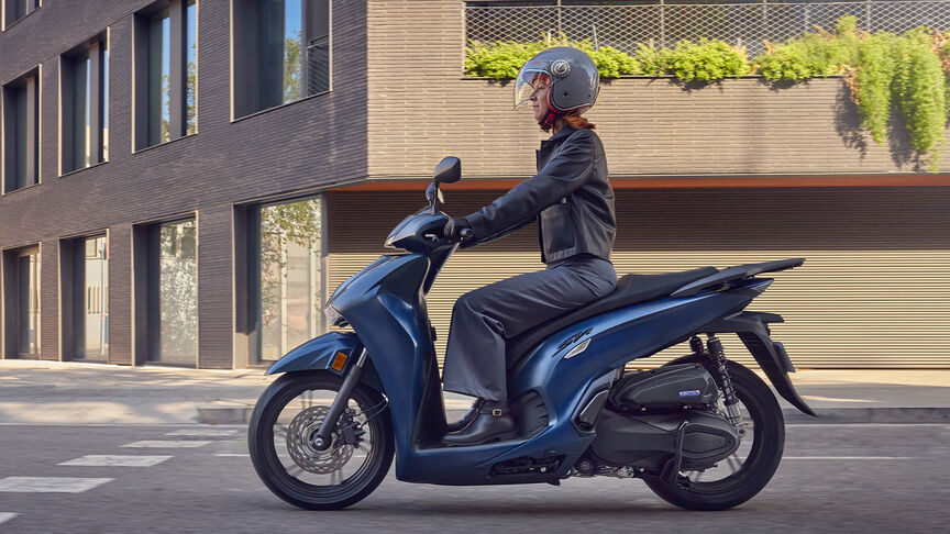 Pohľad zboku na ženu pri jazde na modeli Honda SH350i v meste.