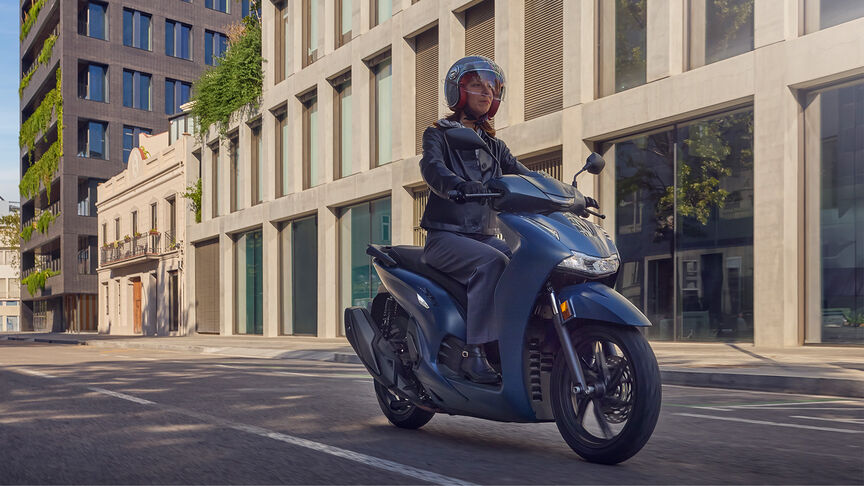 Pohľad zboku na ženu pri jazde na modeli Honda SH350i v meste.